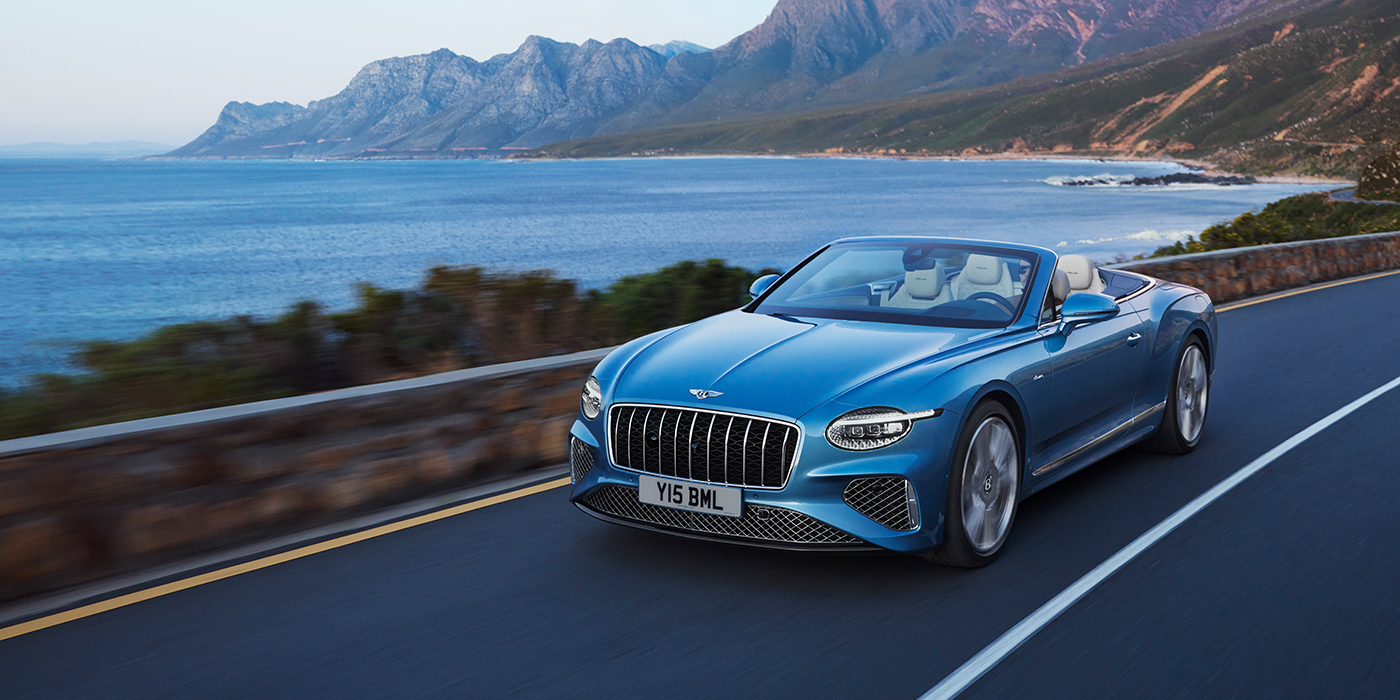 Bentley Praha New Bentley Continental GTC Azure convertible in Light Windsor blue paint with 22 inch Azure wheels and chrome grill, driving dynamically by the sea