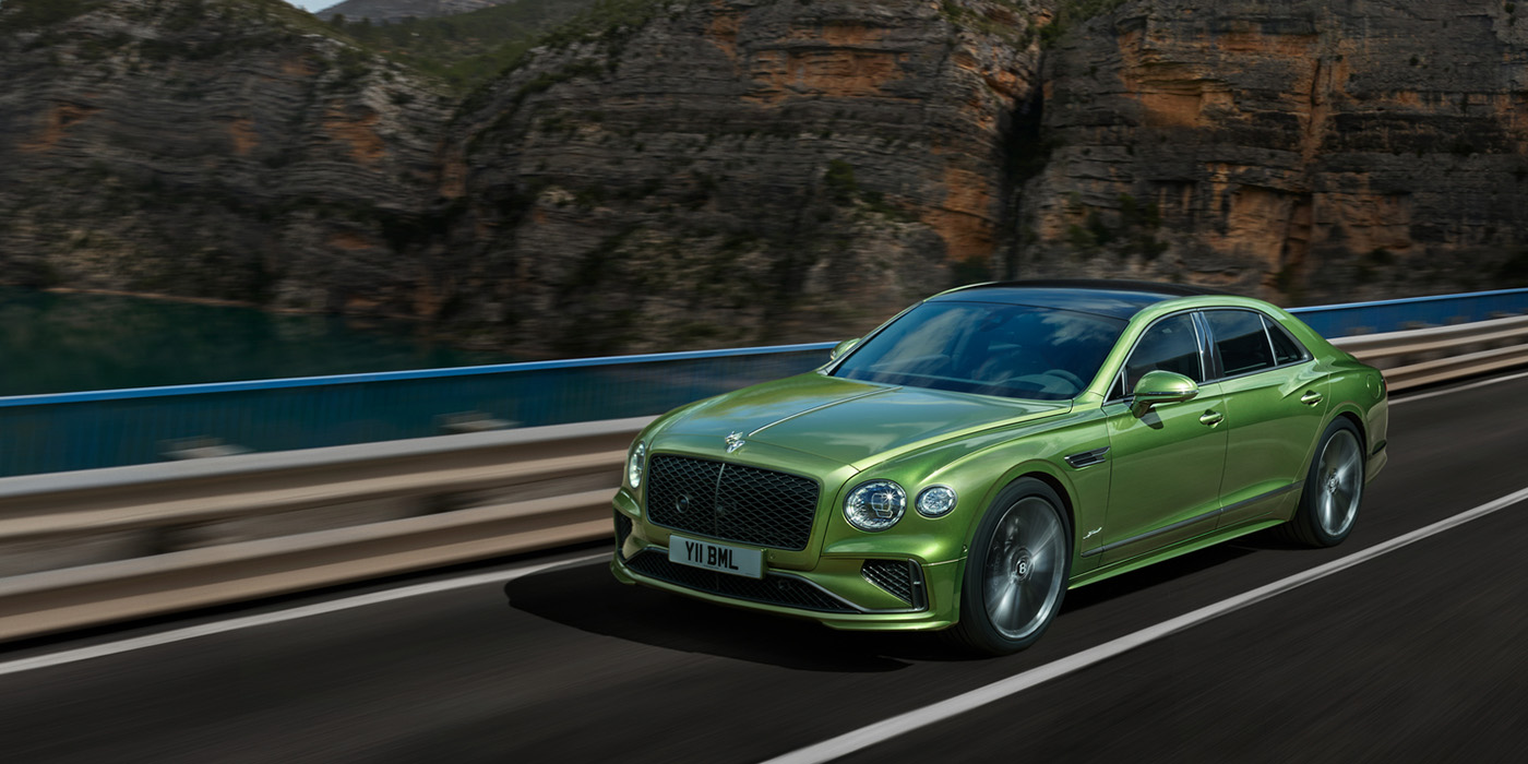 Bentley Praha Bentley New Flying Spur Speed v8 hybrid sedan driving dynamically on a mountain road in Tourmaline Green paint