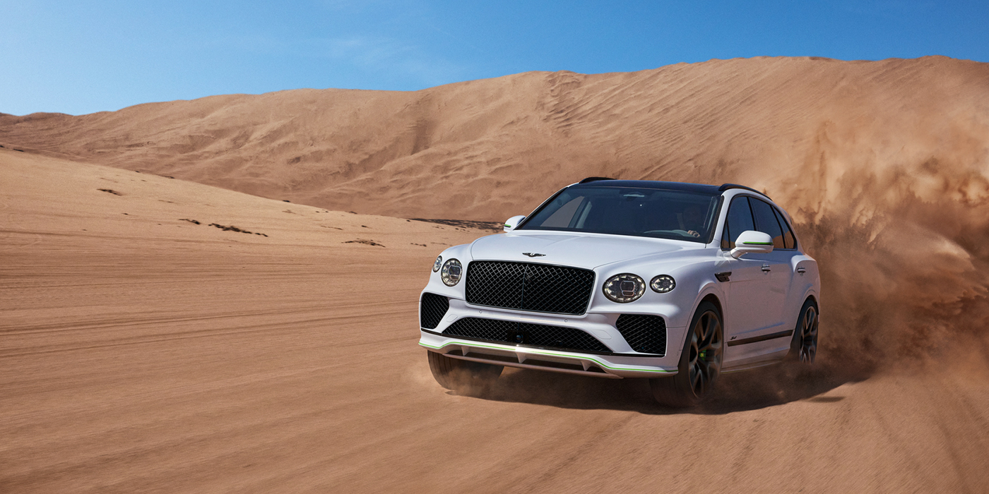 Bentley Praha Bentley Bentayga Speed SUV front three quarter in Snow Quarts Pearlescent by Mulliner white paint driving dynamically through the desert