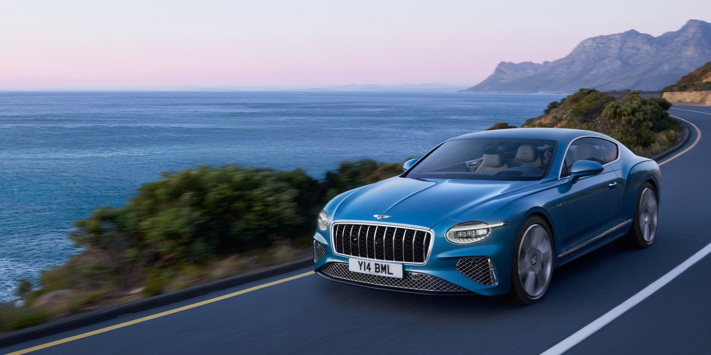 Bentley Praha New Bentley Continental GT Azure coupe in Light Windsor blue paint with 22 inch Azure wheels and chrome grill, driving dynamically by the sea