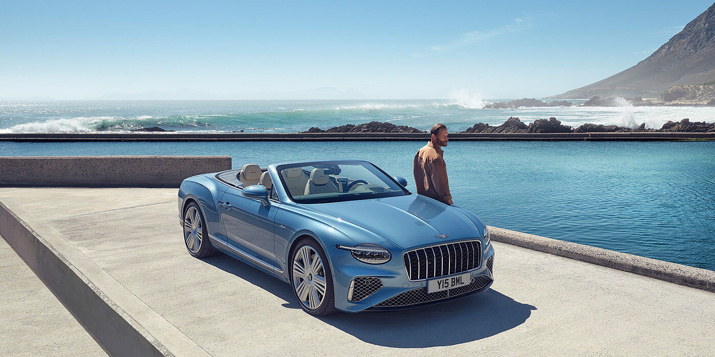 Bentley Praha New Bentley Continental GTC Azure convertible front view in Light Windsor blue paint with 22 inch ten spoke wheels parked by the sea in the sunshine