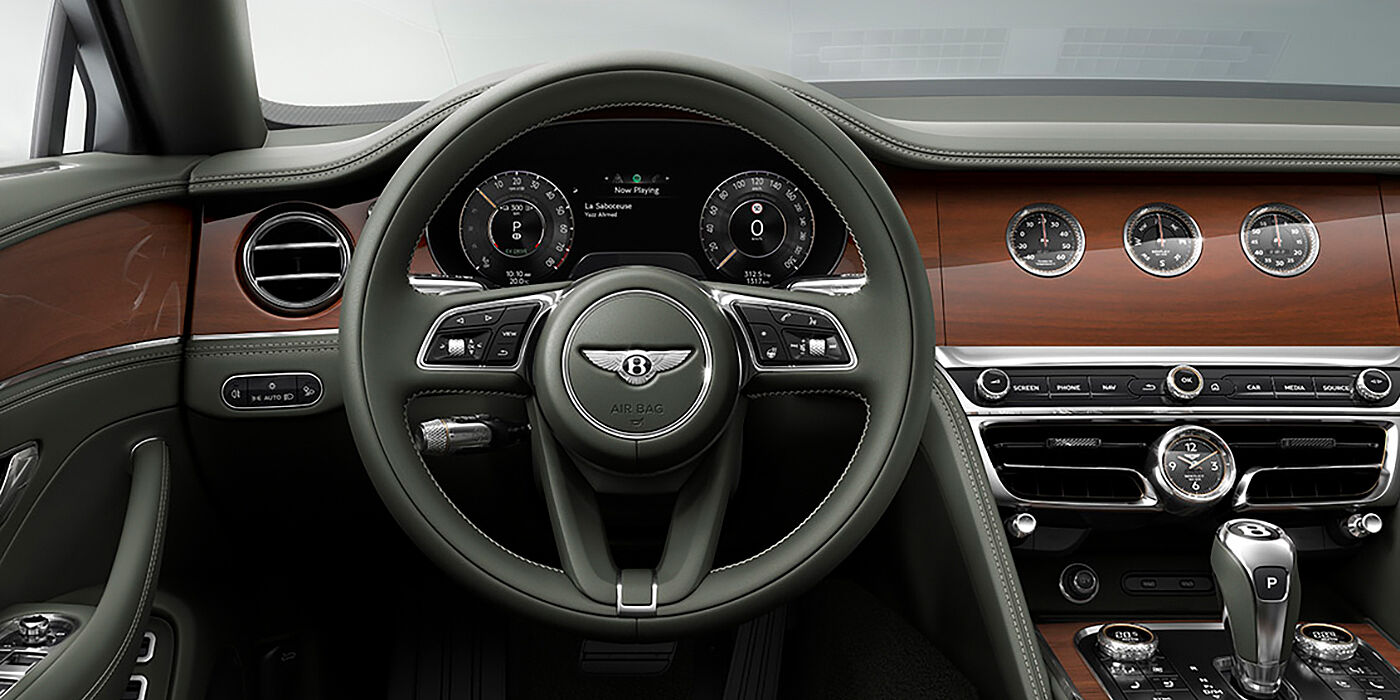 Bentley Praha New Bentley Flying Spur sedan front cabin in Cumbrian Green hide and Crown Cut walnut veneer showing steering wheel and Rotating Display with three clocks on face