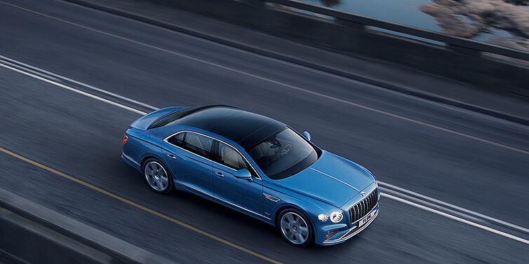 Bentley Praha New Bentley Flying Spur Azure sedan in Light windsor blue paint by Mulliner, with 22 inch Azure wheels seen from overhead driving dynamically on a country road