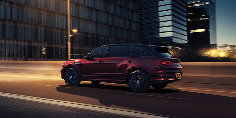 Bentley Praha Bentley Bentayga Extended Wheelbase Mulliner SUV in Cricket Ball red paint driving dynamically in city at night